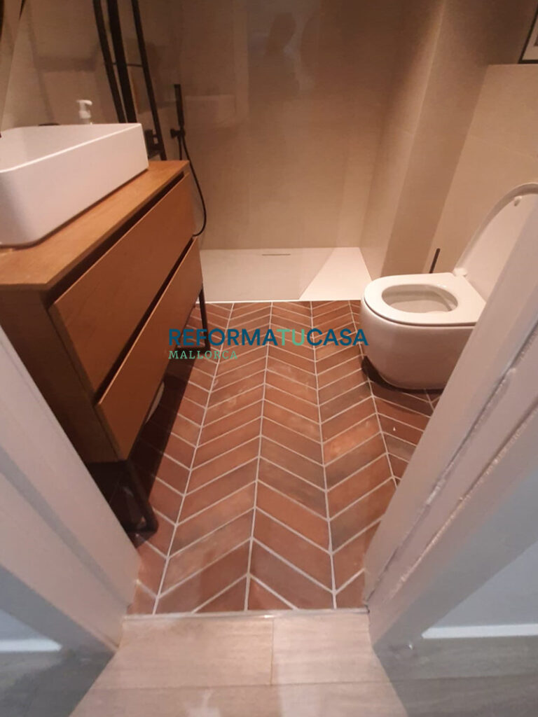 Reforma de baño moderno en Palma de Mallorca con suelo terracota en espiga y mueble de madera.