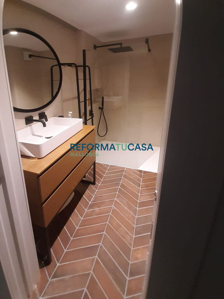 Ducha de obra con grifería negra mate y mampara de vidrio fijo en baño renovado